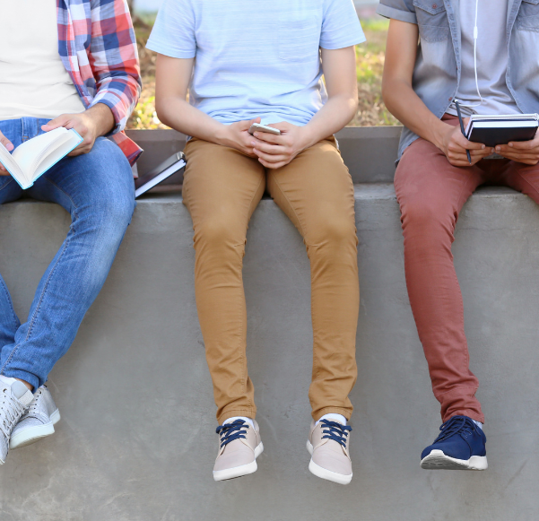 Group of three teens sitting outside. Only their legs are showing