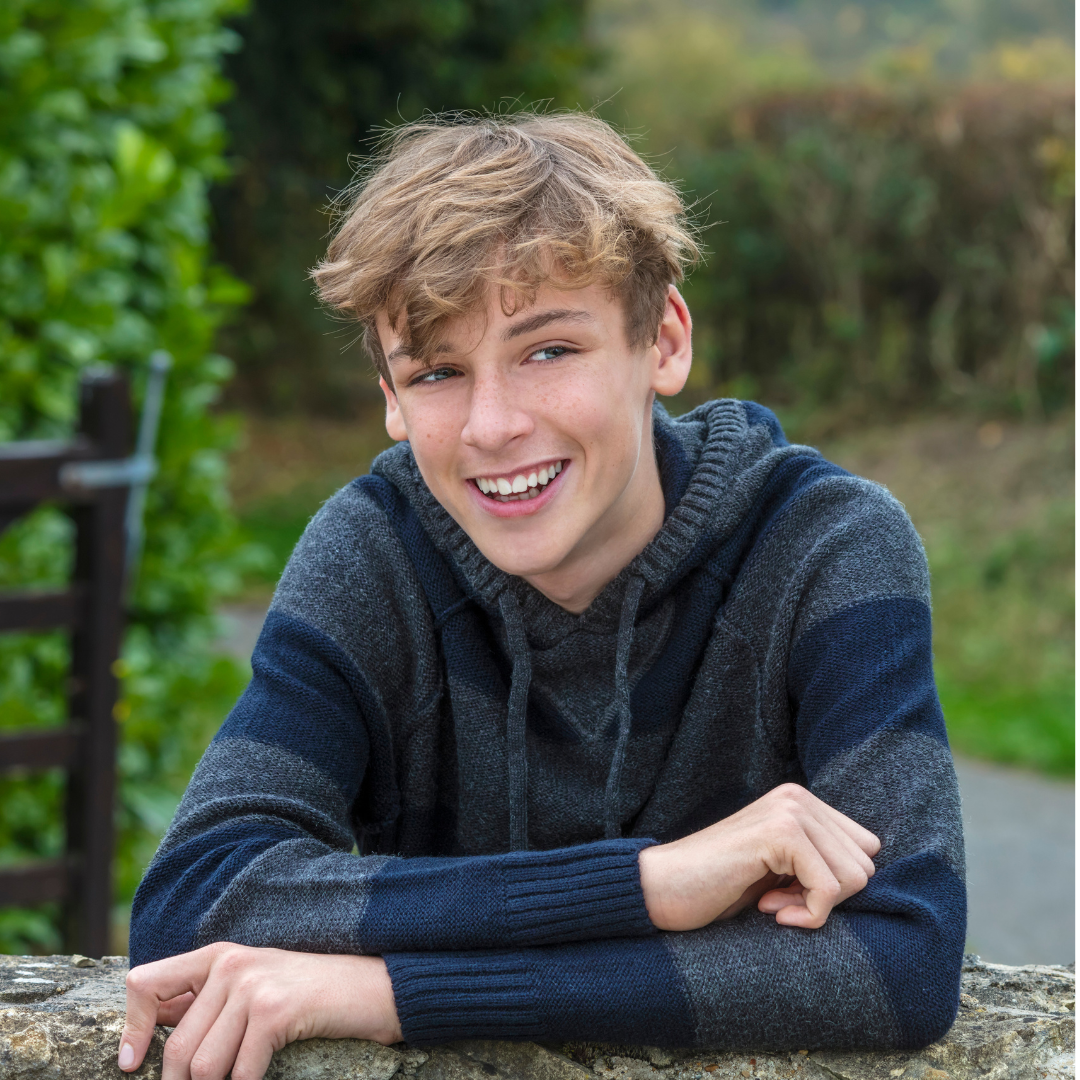 A teen boy is seen smiling outdoors