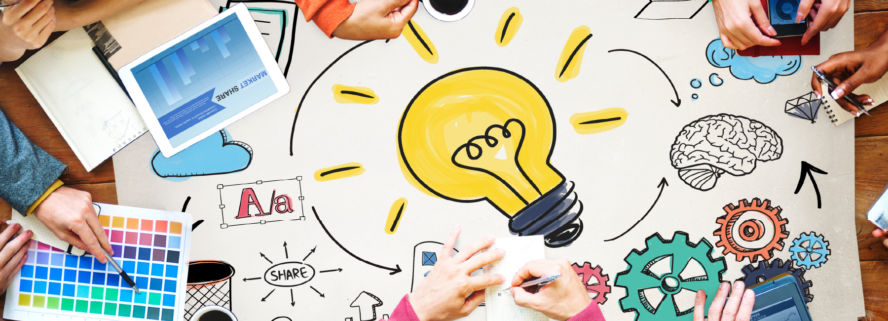 People collaborate around a table with a large paper displaying a lightbulb, gears, and charts, symbolizing brainstorming and innovation